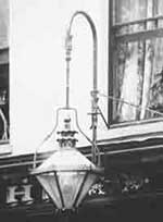 A typical privately-owned gas lamp suspended outside, over a shop window and contributing 
		to the illumination of the streets in the early 1900s.